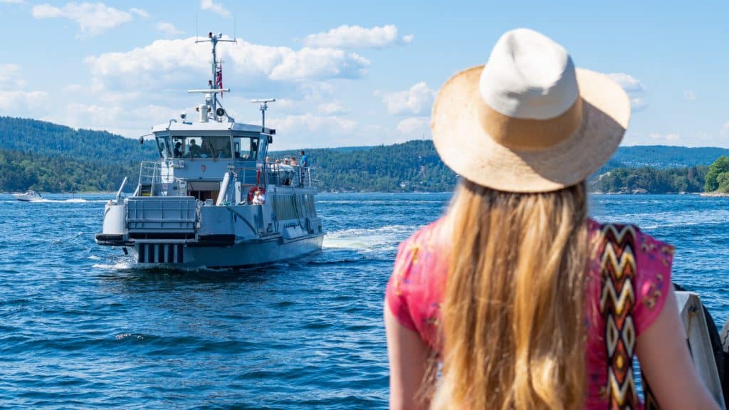 Dame som venter på Oscarsborgfergen med hatt en solrik dag