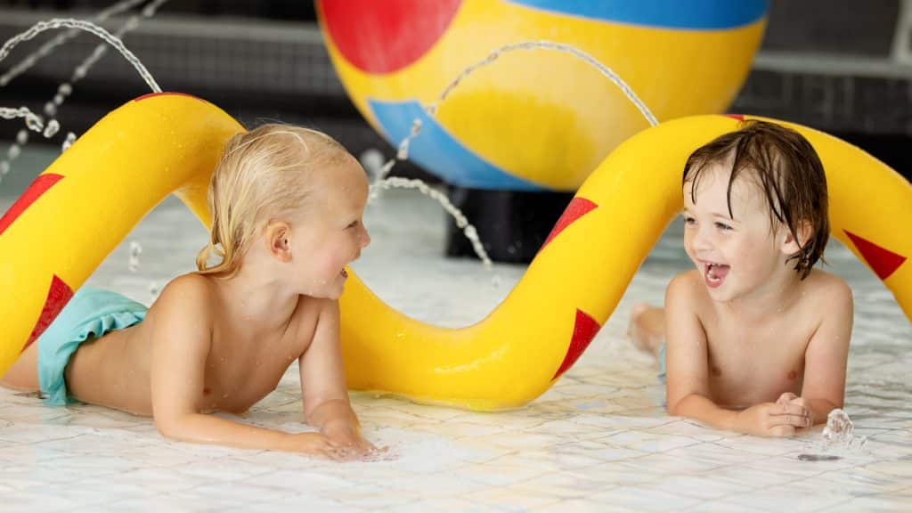 To barn som leker i barnebasseng med gule leker bak seg