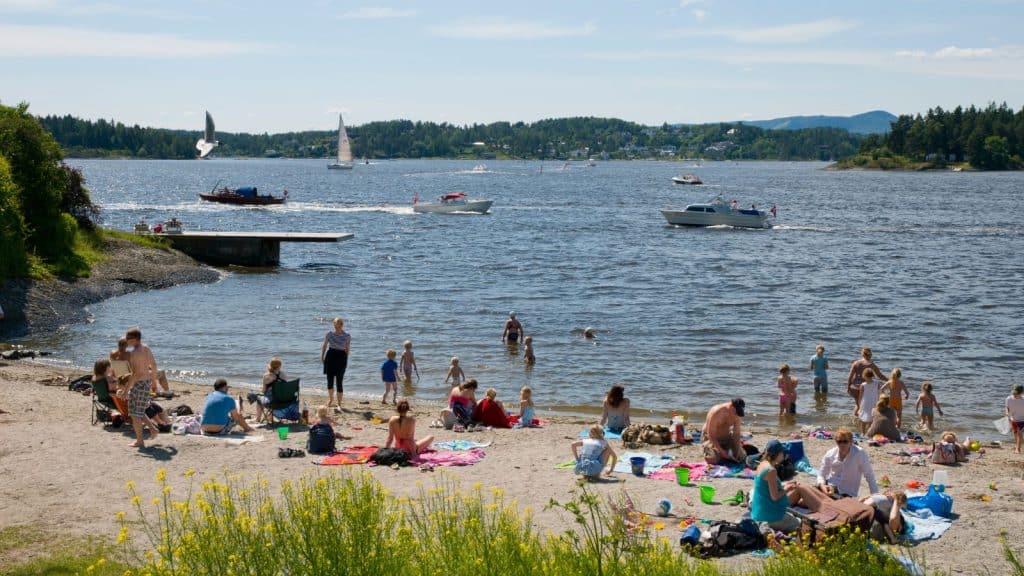 Folk som koser seg i sola på en liten strand båter kjører på. vannet i bakgrunnen