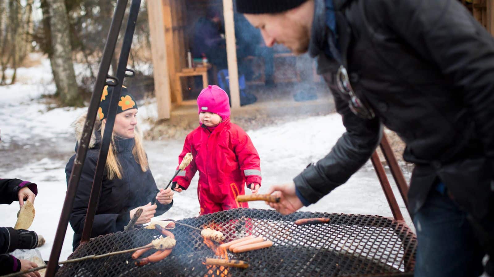 Mann og dame griller pølser til et lite barn i rosa dress