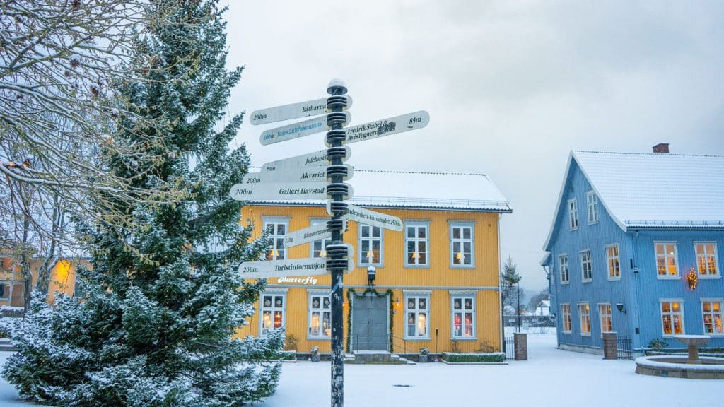Juletre på et torg i vinterdrakt med et gult og et blått trehus i bakgrunnen