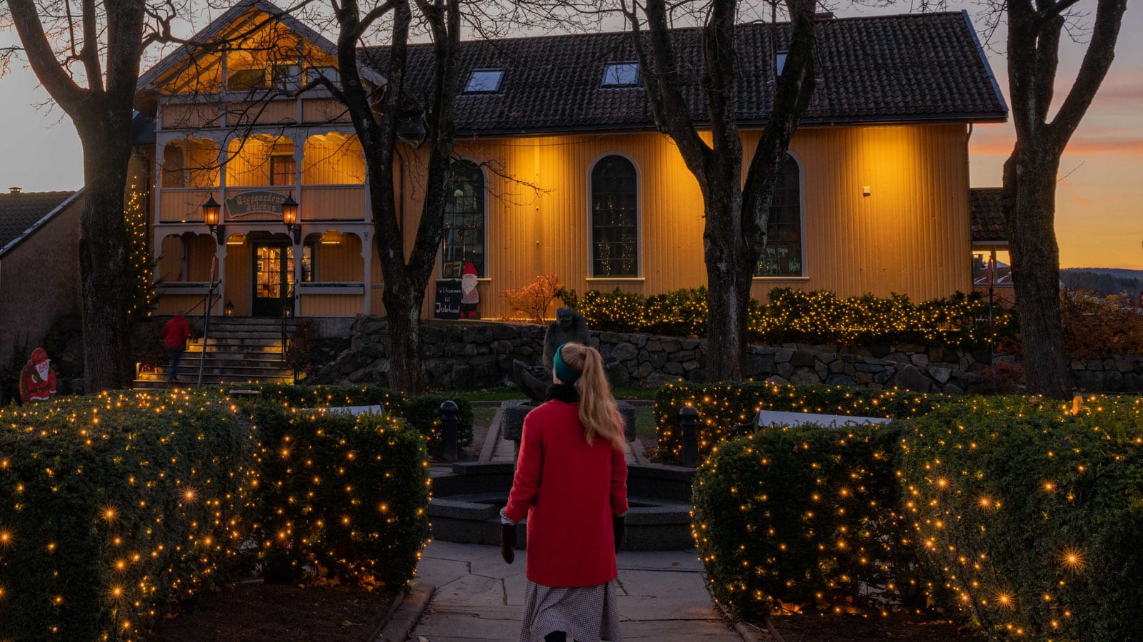 Dame som går utenfor et gult trehus i juletider