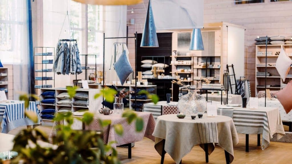 Interiørbilde fra Klässbols Linneväveri med bord dekket av mønstrede duker, dekorasjoner, tekstiler på hyller og moderne belysning