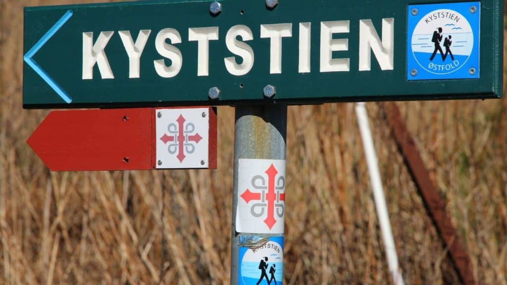 Grønt skilt med teksten «Kyststien» og blå pil, samt turmerking for fotturer i Østfold.