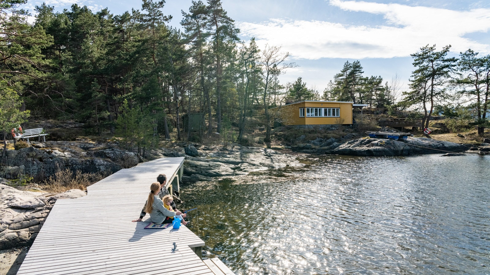Mor far og datter som fisker krabber på en brygge ved en gul hytte ved fjorden