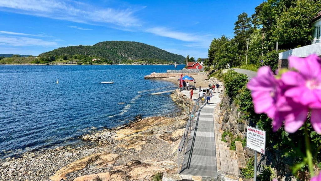 Strand med rullestolrampe med fjord i bakgrunn og steinstrand