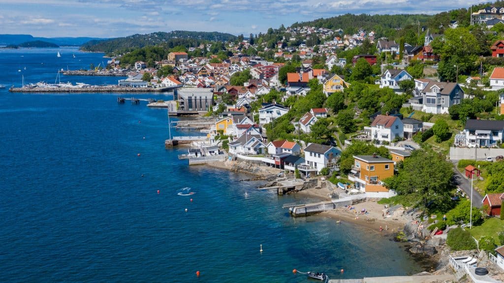 Dronebilde av strand og by langs Oslofjorden en solfylt sommerdag med blått vann