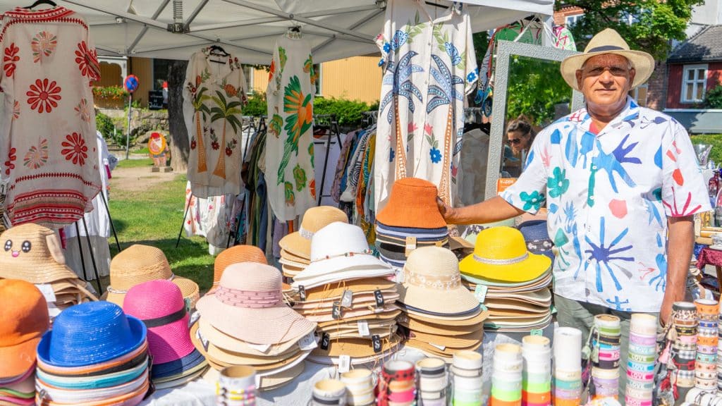 Mann med hatt som selger hatter og tunikaer på et torg