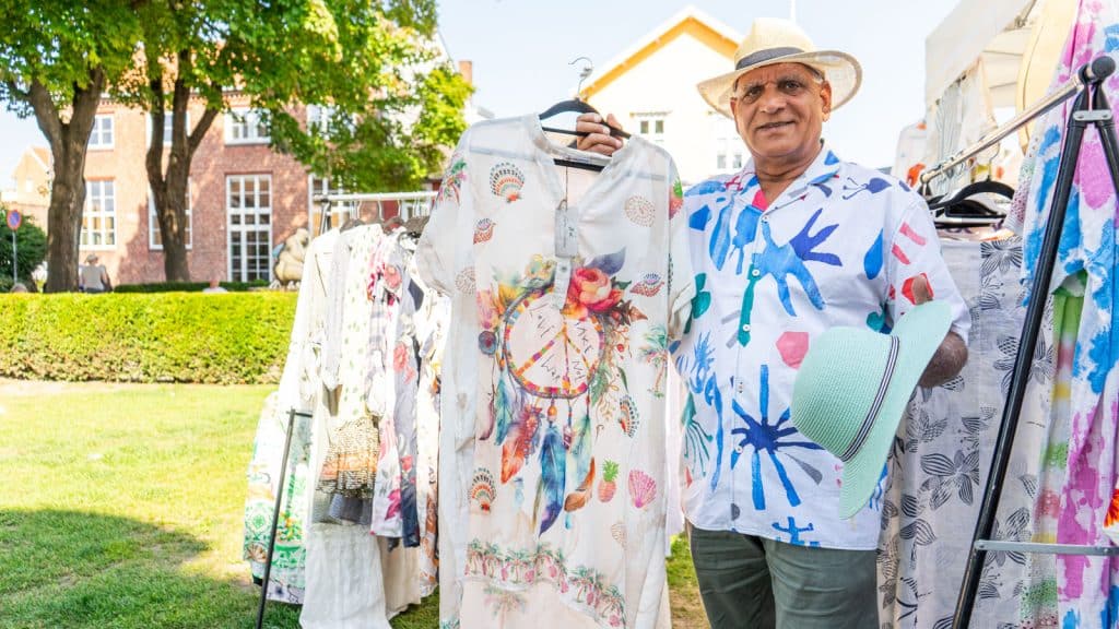 Man wearing a hat and selling tunics in a market square in summer