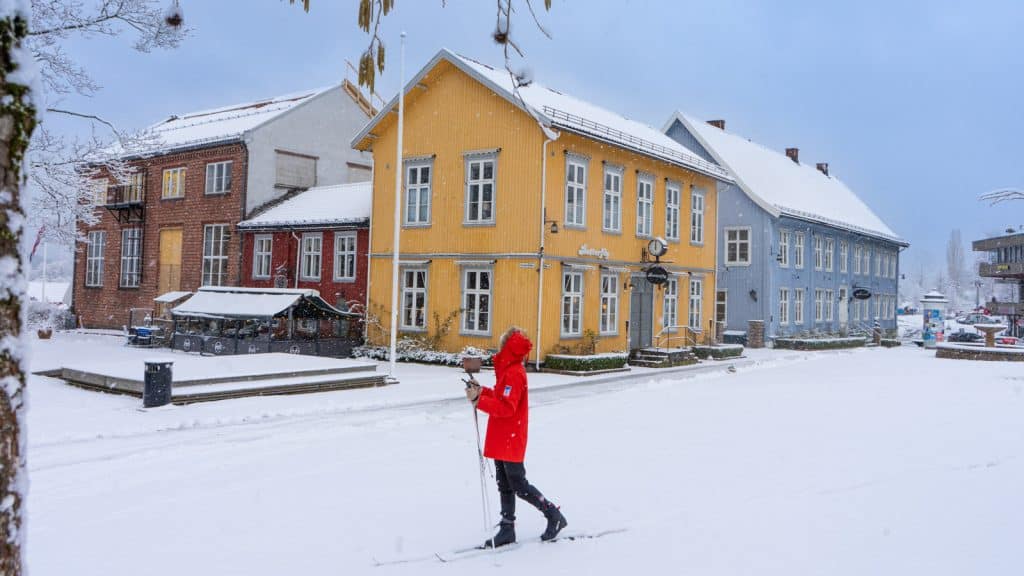 Jente som går på ski i anorakk på et torg med trehus