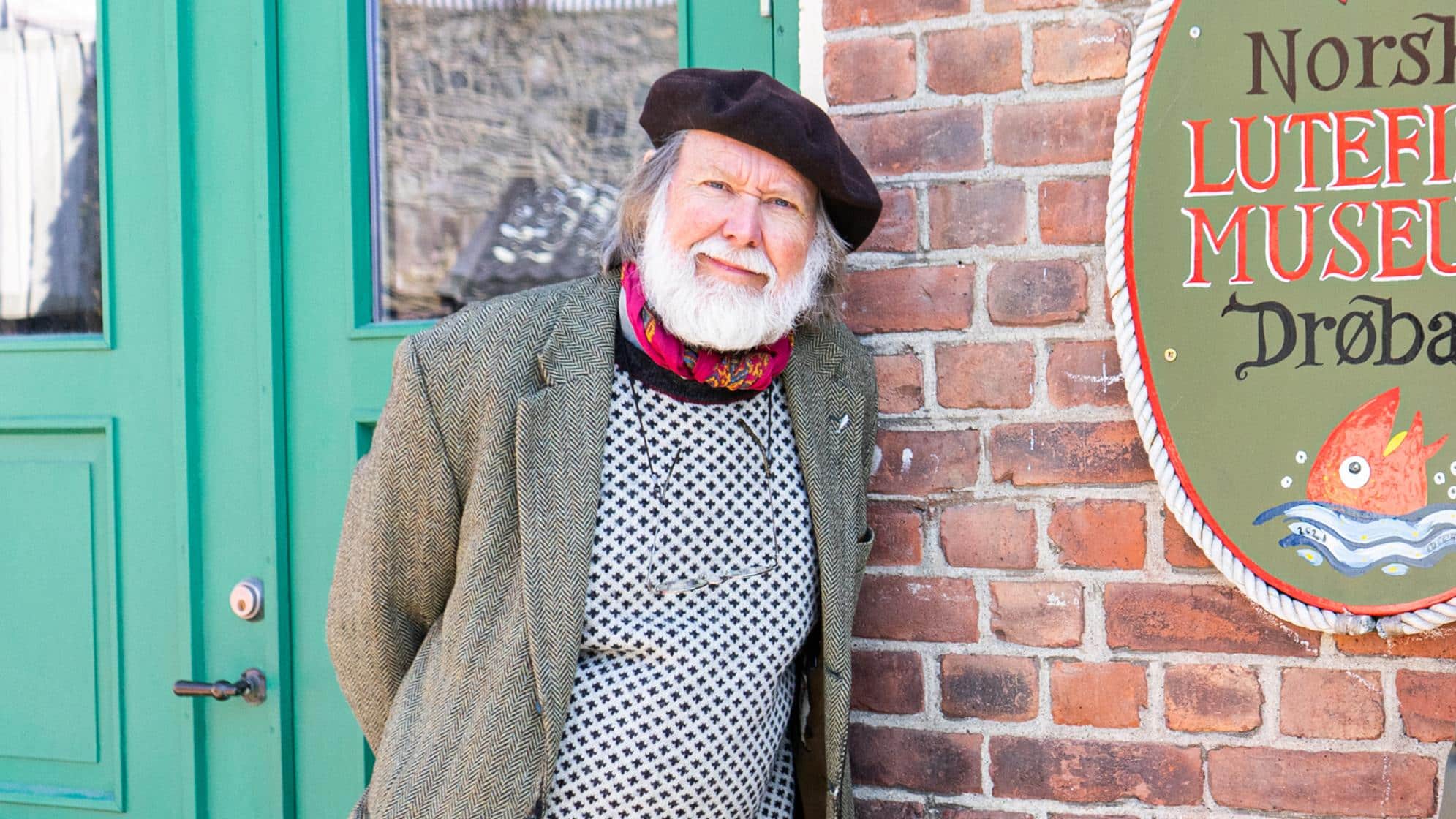 Mann med beret foran et murhus