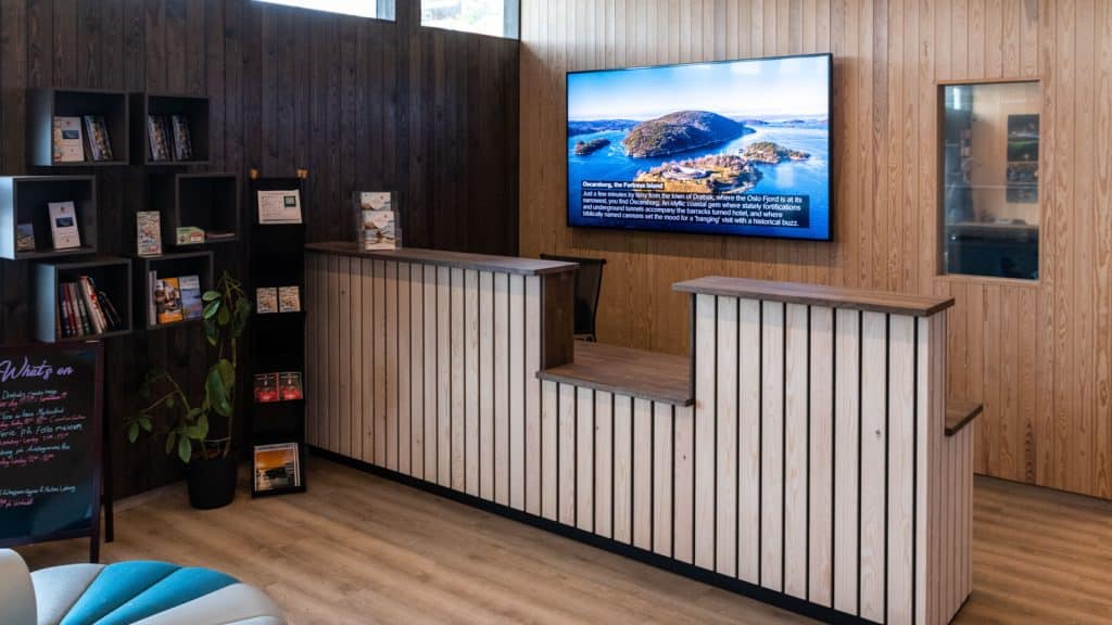 Resepsjonsdisk i tre med stor tv og brosjyrestativ