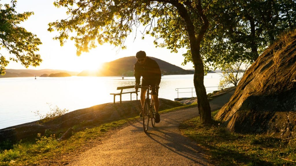 Mann som sykler i solnedgang ved fjorden