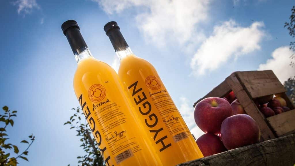 2 flasker med gult innhold og epler ved siden av