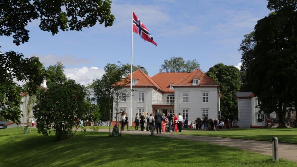 Hvit store bygning med mennesker foran med fladd, eidsvollbygningen